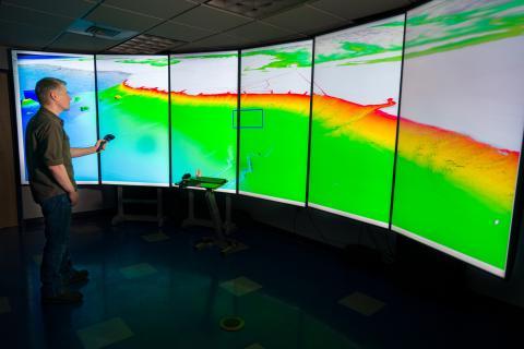 Presenter at a surround-screen digital map showing topography.